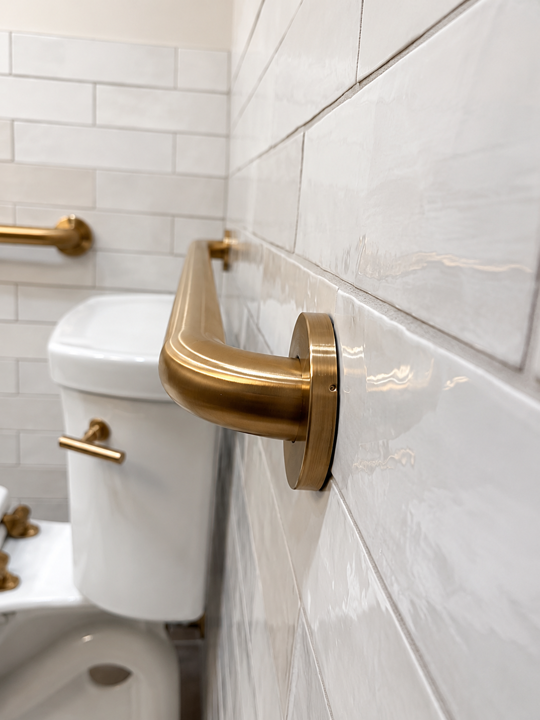 ADA bathroom with gold grab bars, white subway tile, and wood-look flooring