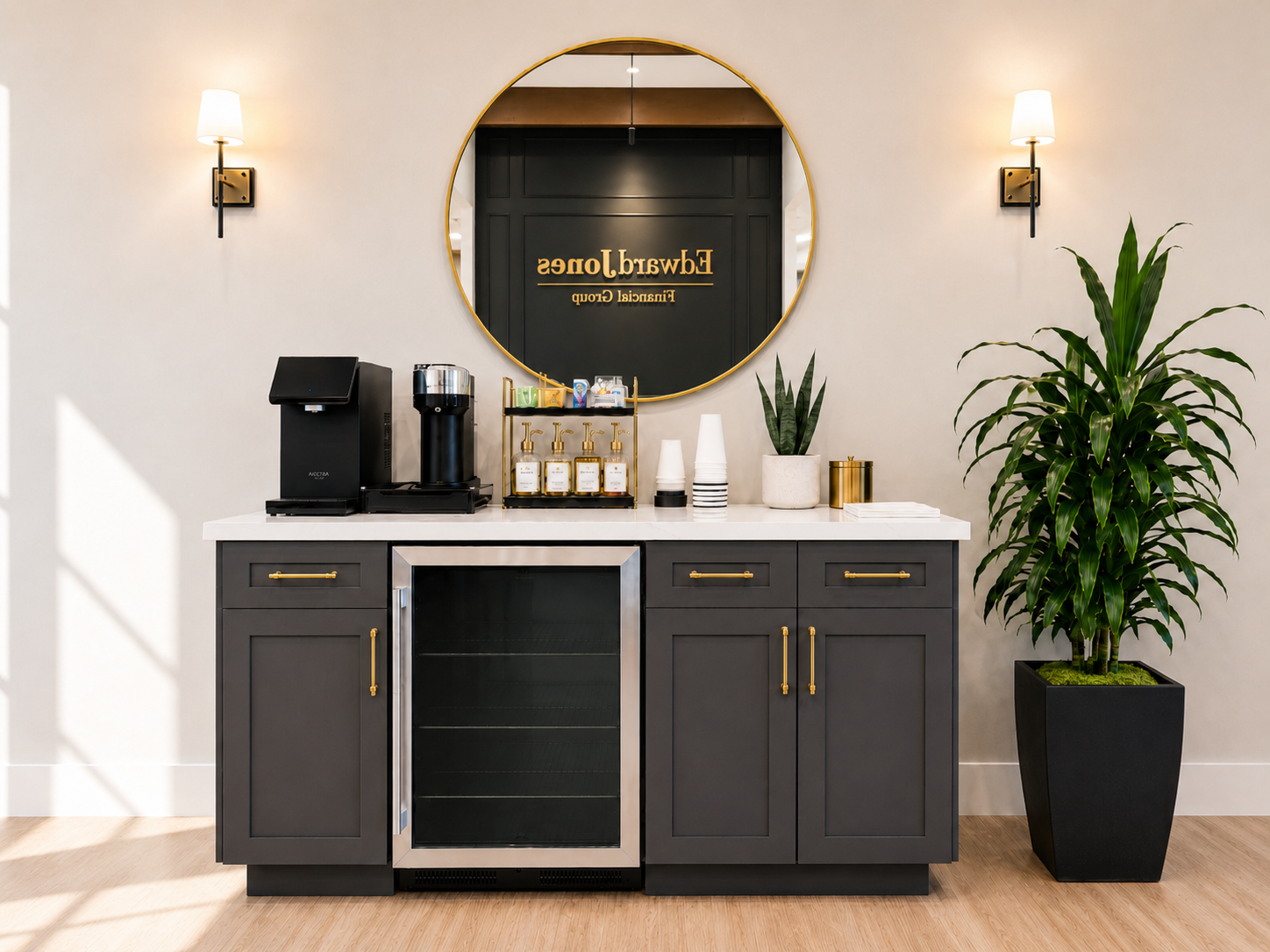 Lobby beverage station with dark cabinetry, gold hardware, and round mirror